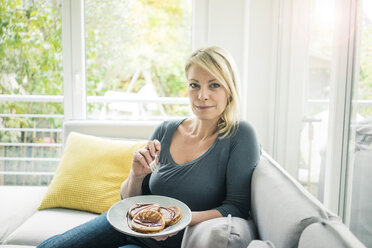 Portrait of woman sitting on couch eating pancakes - MOEF00286