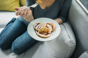 Nahaufnahme einer Frau, die auf der Couch sitzt und Pfannkuchen isst - MOEF00287