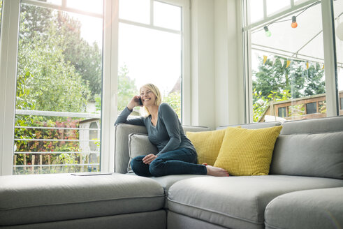 Glückliche Frau beim Telefonieren auf der Couch - MOEF00289