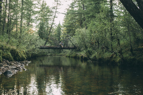 Mann sitzt auf einem Baumstamm über einem Fluss im Wald - VPIF00240