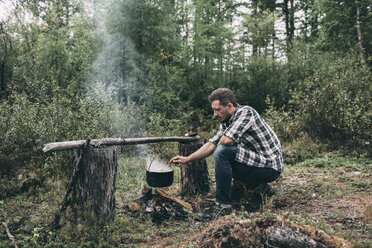 Man cooking in cauldron in rural landscape - VPIF00259