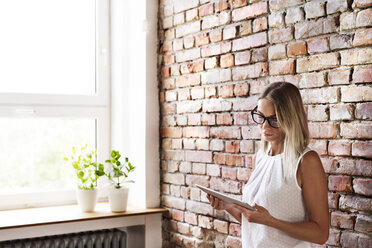 Businesswoman using tablet at brick wall in office - HAPF02341