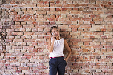 Businesswoman using cell phone at brick wall - HAPF02346