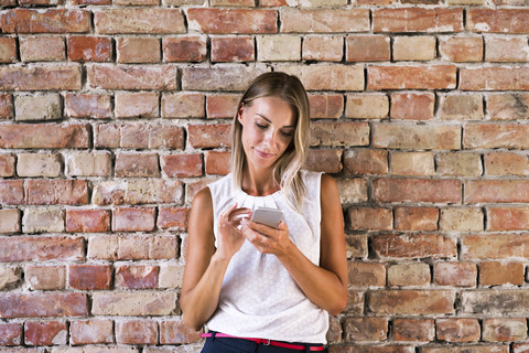 Geschäftsfrau mit Mobiltelefon an einer Ziegelmauer, lizenzfreies Stockfoto