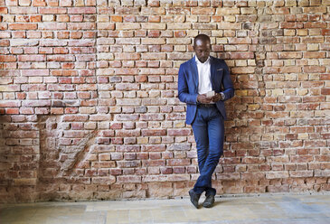 Businessman using cell phone at brick wall - HAPF02353