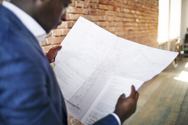 Businessman studying construction plan at brick wall - HAPF02366