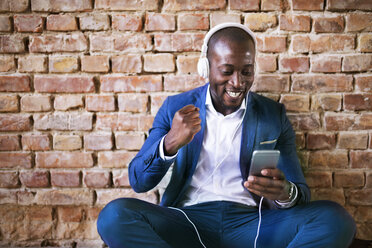 Happy businessman with headphones and smartphone cheering - HAPF02370