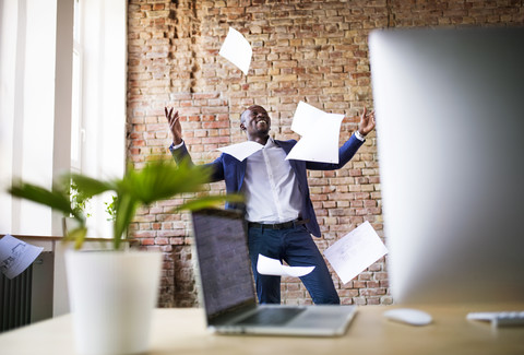 Sorgloser Geschäftsmann im Büro, der Papiere wegwirft, lizenzfreies Stockfoto