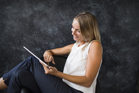 Lächelnde Geschäftsfrau, die in einem Sessel sitzt und ein Tablet benutzt, lizenzfreies Stockfoto