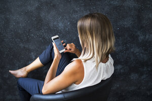 Geschäftsfrau im Sessel sitzend, die Daten auf dem Mobiltelefon überprüft - HAPF02387