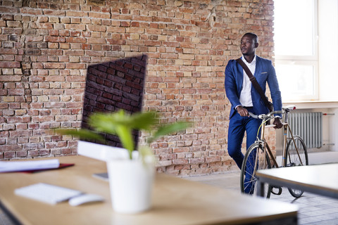 Geschäftsmann schiebt Fahrrad im Büro, lizenzfreies Stockfoto