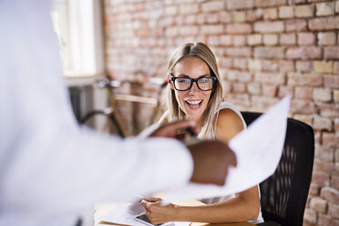 Colleague showing paper to happy woman at desk in office - HAPF02407