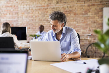 Businessman using laptop in office with colleagues in background - HAPF02416