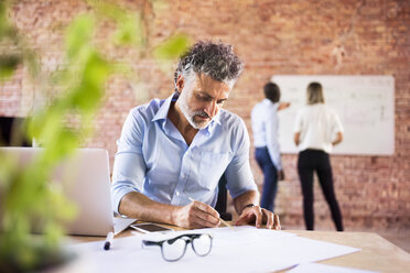 Businessman working in office with colleagues in background - HAPF02427