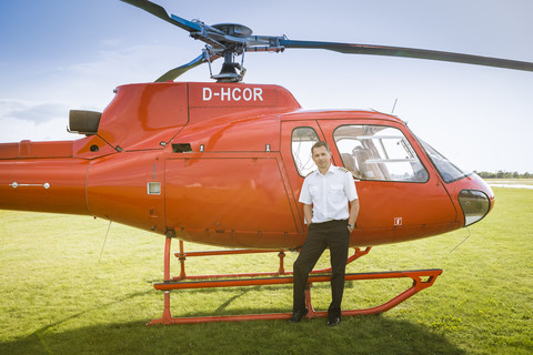 Porträt eines Piloten, der neben einem roten Hubschrauber steht, lizenzfreies Stockfoto