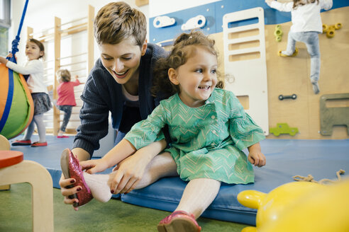 Pre-school teacher helping little girl putting a shoe on - MFF04052