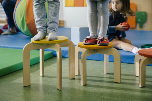 Feet of two children standing on chairs of different heights in kindergarten - MFF04055