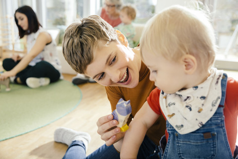 Pre-school teacher playing with toddler in kindergarten stock photo