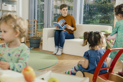 Vorschullehrerin mit Buch, die sich Kinder im Kindergarten ansieht, lizenzfreies Stockfoto