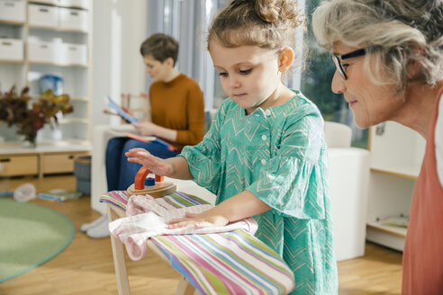 Teacher watching girl ironing in kindergarten - MFF04075