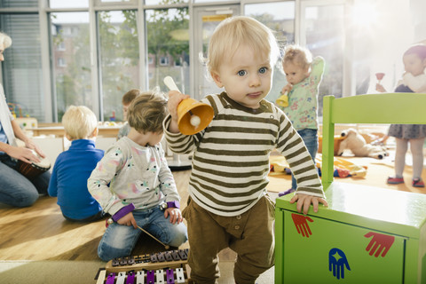 Kleinkind, das im Musikzimmer eines Kindergartens eine Glocke läutet, lizenzfreies Stockfoto