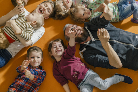 Children and teachers lying and singing on carpet in kindergarten stock photo