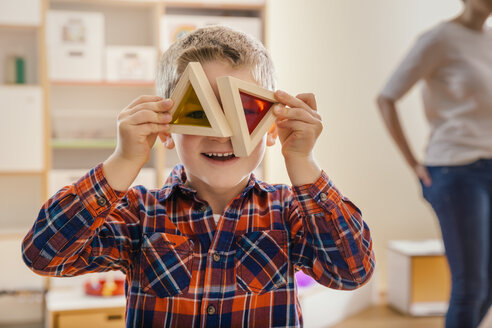 Junge hält hölzerne und bunte Klötze vor seinen Augen im Kindergarten - MFF04088