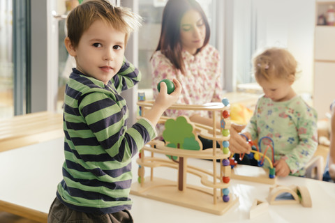 Junge schaut vom Spielen mit Spielzeug im Kindergarten auf, lizenzfreies Stockfoto