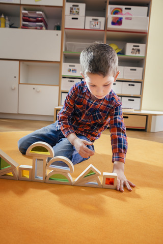 Junge reiht Holzspielzeugformen auf Teppich im Kindergarten auf, lizenzfreies Stockfoto