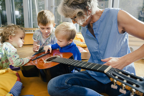 Vorschullehrerin zeigt Kindern im Kindergarten eine Gitarre, lizenzfreies Stockfoto