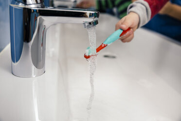 Child cleaning his toothbrush in bathroom of a kindergarten - MFF04102