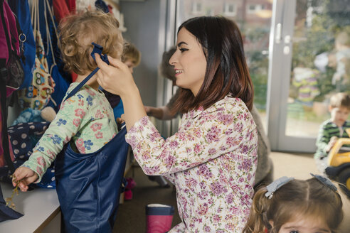 Vorschullehrerin hilft Mädchen beim Anziehen der Matschhose im Kindergarten - MFF04107