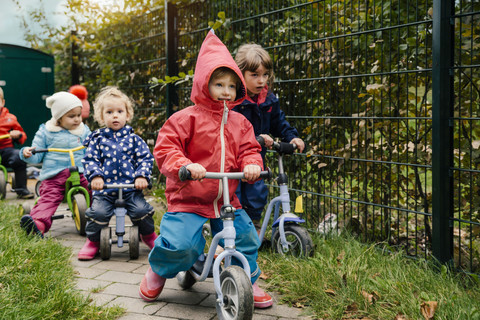 Kinder auf Rollern im Garten eines Kindergartens, lizenzfreies Stockfoto