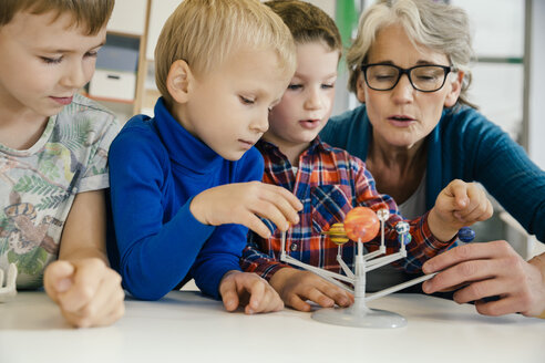 Pre-school teacher explaining solar system model to boys in kindergarten - MFF04124