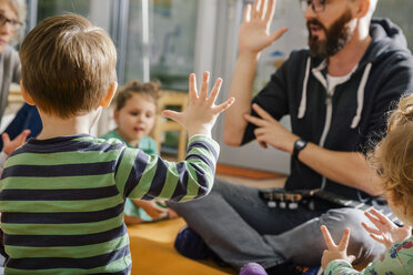 Kind hebt die Hand beim Singen mit anderen und der Lehrerin im Kindergarten - MFF04143
