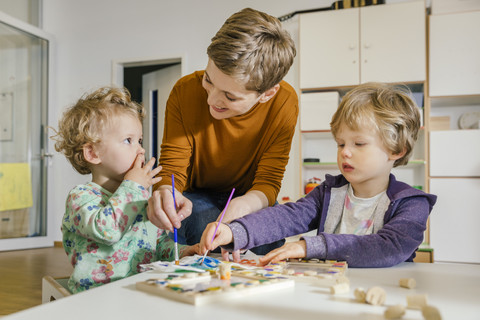 Pre-school teacher painting with two children in kindergarten stock photo