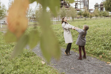 Mutter und kleine Tochter tanzen zusammen auf einem Spazierweg im Herbst - KMKF00052