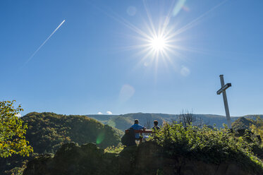 Deutschland, Rheinland-Pfalz, Ahrtal, Altenahr, Rotweinwanderweg, Seniorenehepaar sitzt neben Gipfelkreuz, gegen die Sonne - FRF00592