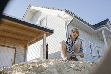 Portrait of blond boy playing near construction site of a detached one-family house - KMKF00054