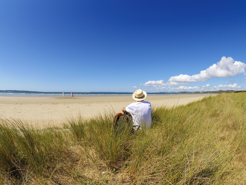 Frankreich, Bretagne, älterer Mann, der eine Pause am Strand macht, auf einer Düne sitzend, lizenzfreies Stockfoto