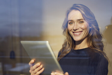 Porträt einer lachenden Frau mit Tablet hinter einer Fensterscheibe - PNEF00245