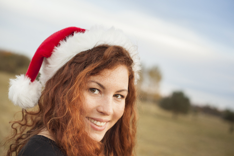Porträt einer rothaarigen jungen Frau mit Weihnachtsmütze in der Natur, lizenzfreies Stockfoto