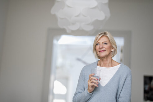 Porträt einer entspannten älteren Frau mit einem Glas Wasser zu Hause - FMKF04613