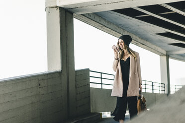 Smiling young woman with cell phone wearing wooly hat - UUF12209