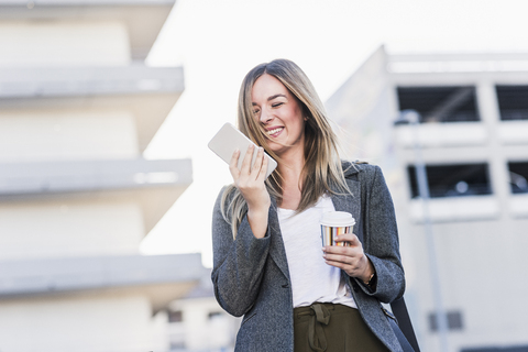 Glückliche junge Frau mit Kaffee zum Mitnehmen und Mobiltelefon in der Stadt, lizenzfreies Stockfoto
