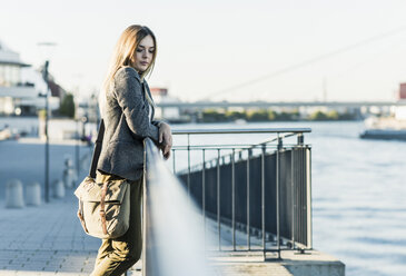 Thoughtful young woman leaning on railing at the riverside - UUF12223