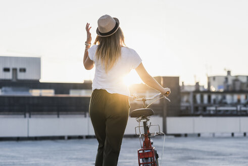 Junge Frau schiebt ihr Fahrrad auf einem Parkdeck bei Sonnenuntergang - UUF12231
