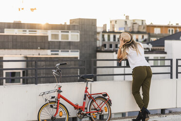 Junge Frau mit Fahrrad, die sich an ein Geländer lehnt - UUF12232