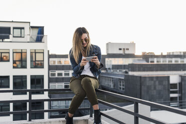 Lächelnde junge Frau in der Stadt, die ihr Handy am Geländer überprüft - UUF12237