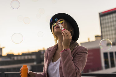Young woman in the city blowing soap bubbles in the evening - UUF12240